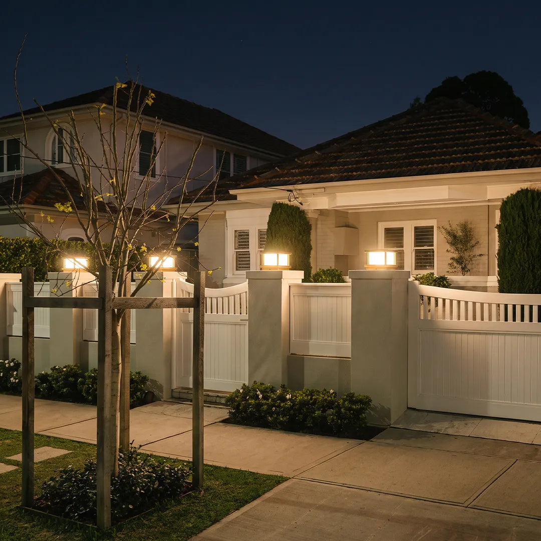 Modern outdoor pillar lights illuminating white fence and residential driveway