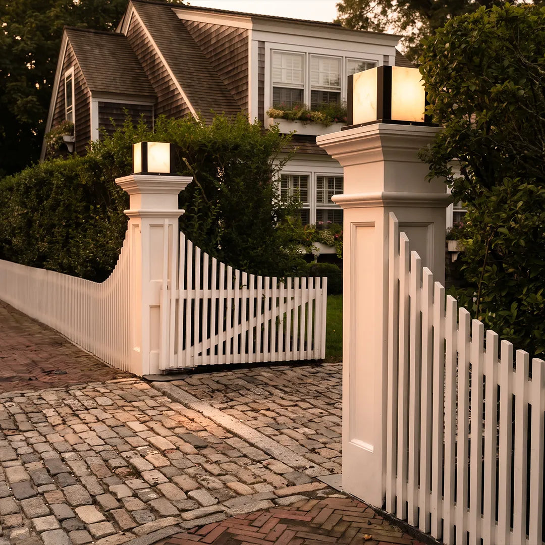 Modern outdoor pillar lights with warm glow on white gate columns beside home