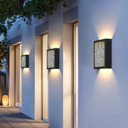 Exterior wall with mounted modern outdoor sconces black fixtures casting warm patterned light.
