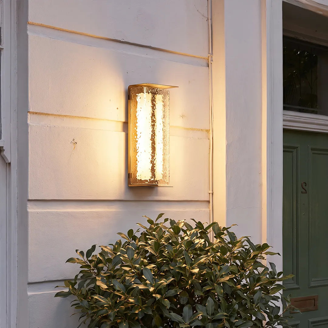 Modern outdoor solar wall lights installed on white siding above shrubs near a house corner.