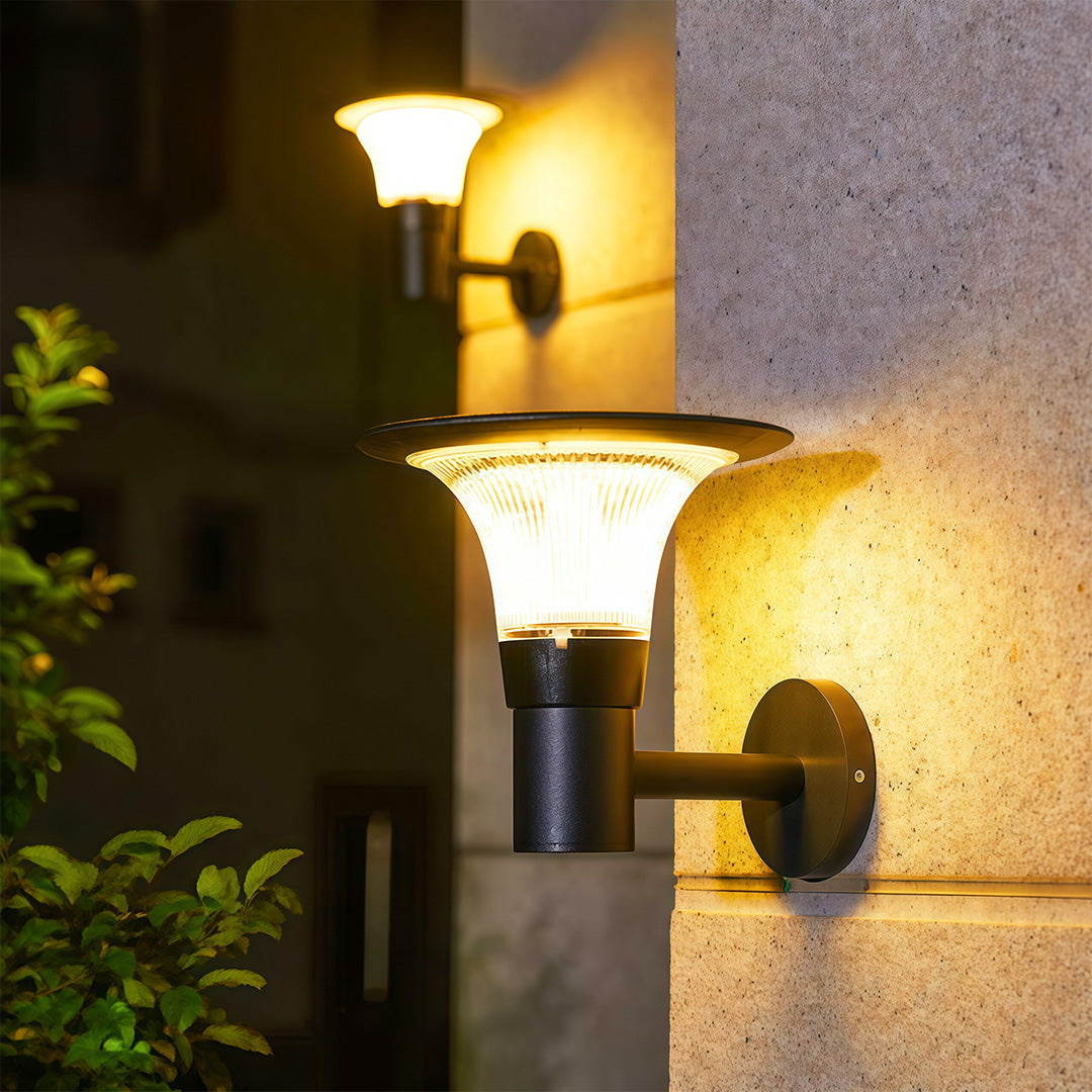 Modern outdoor solar wall sconce with a 'halo' solar panel, casting a warm yellow glow on a textured wall.