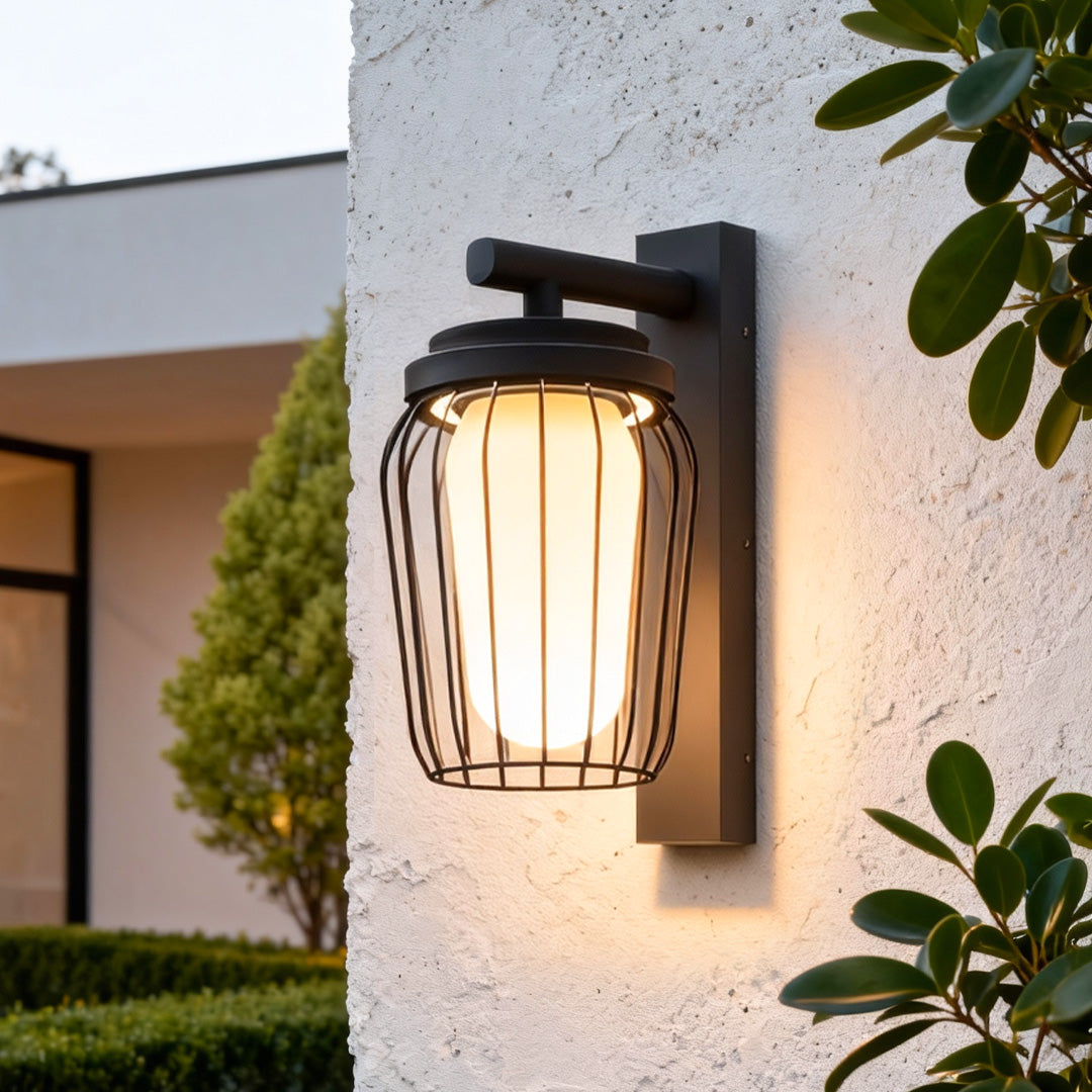 Modern outdoor wall lantern sconce with ribbed glass shade installed on a white textured wall at sunset.