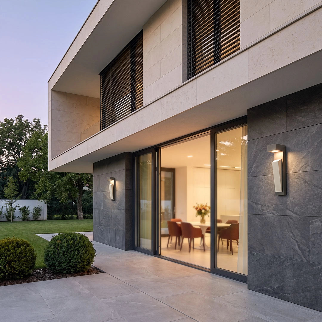 Modern outdoor wall light illuminating the exterior of a contemporary house with large windows.