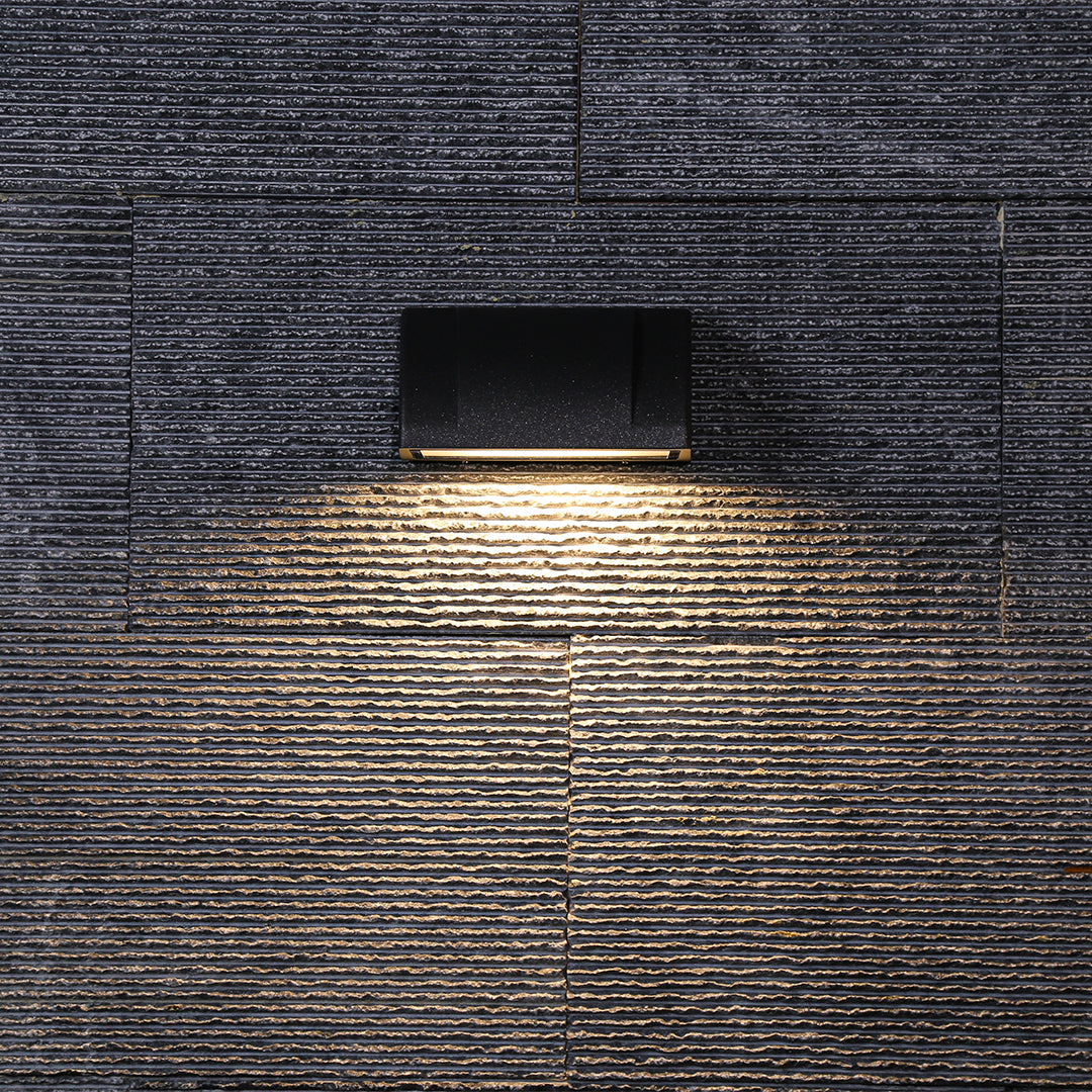 Single modern outdoor wall light casting a clean, even glow across a dark textured exterior surface.