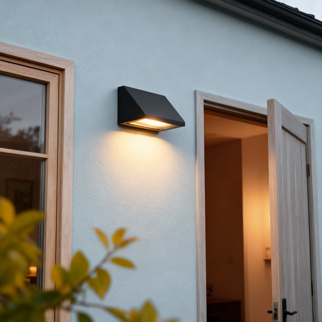 Modern outdoor wall light installed beside an exterior door, casting a warm downward glow on a light-colored wall.