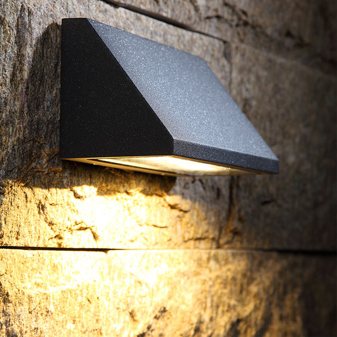 Close-up of a modern outdoor wall light with matte black finish and integrated LED panel for downward lighting.