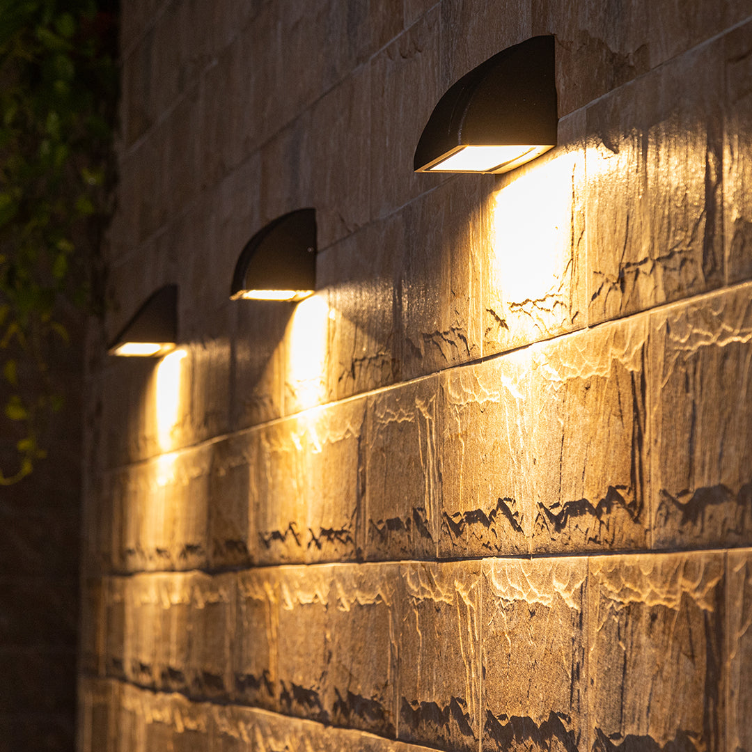 Modern outdoor wall light arranged in a row along a stone wall, providing consistent warm accent lighting at night.