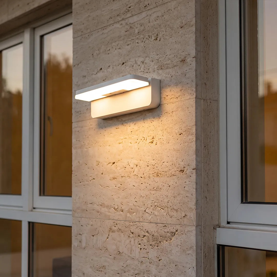 Modern outdoor wall light with warm glow on stone wall beside glass windows