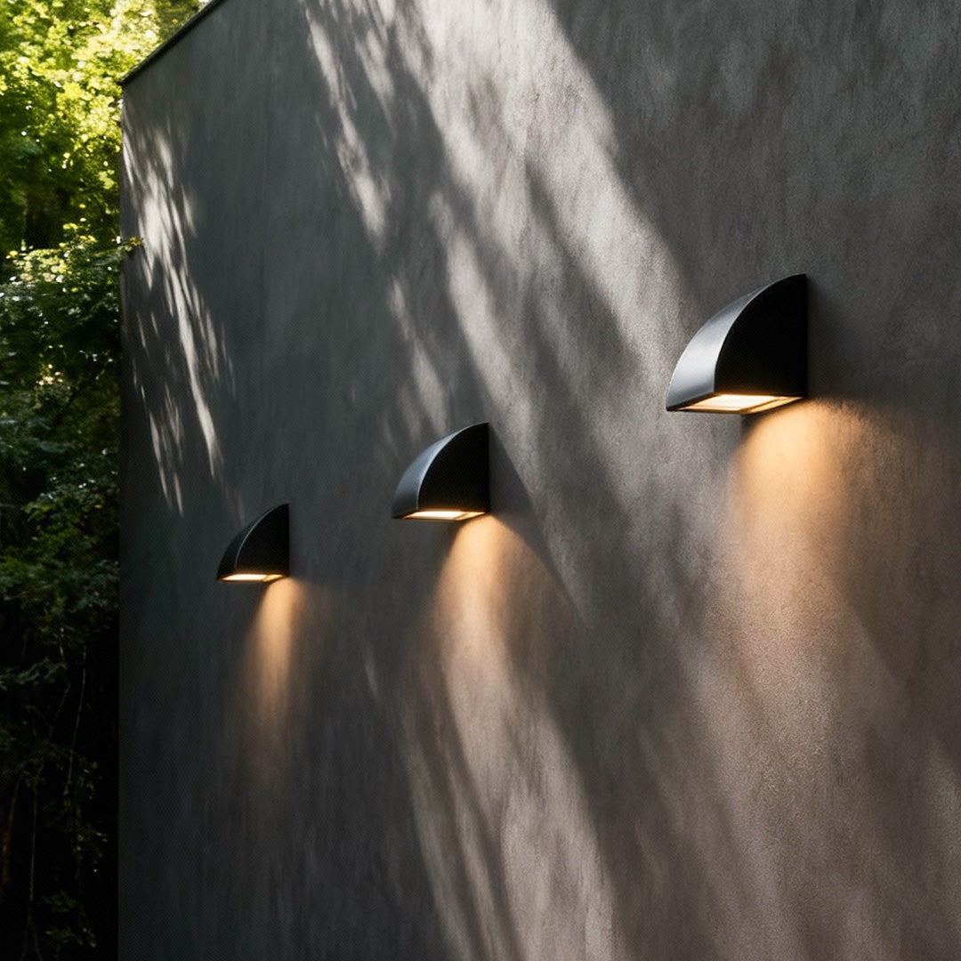 Modern outdoor wall light mounted on a textured exterior wall, creating soft ambient lighting along a pathway.