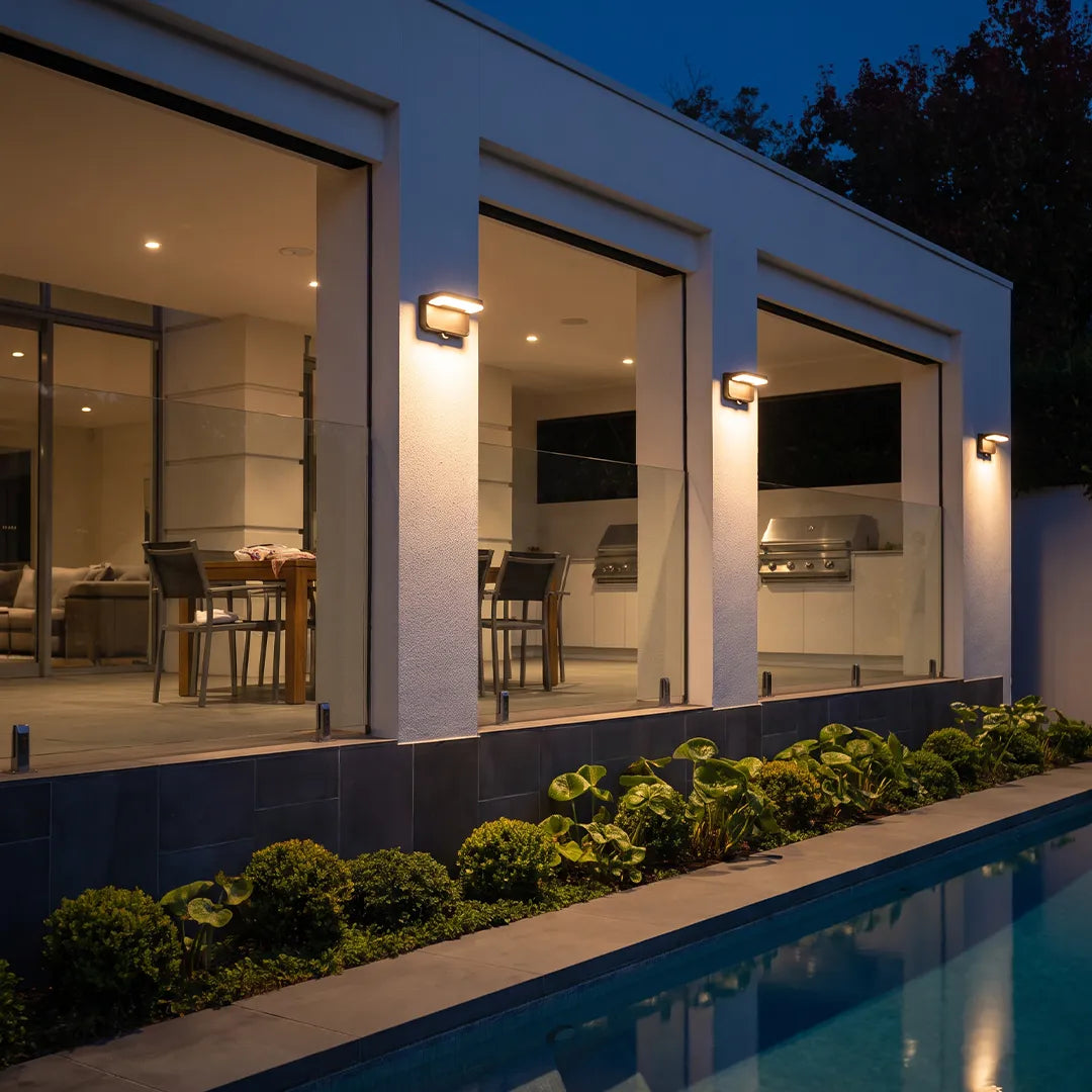 Modern outdoor wall lights with warm glow along poolside home exterior