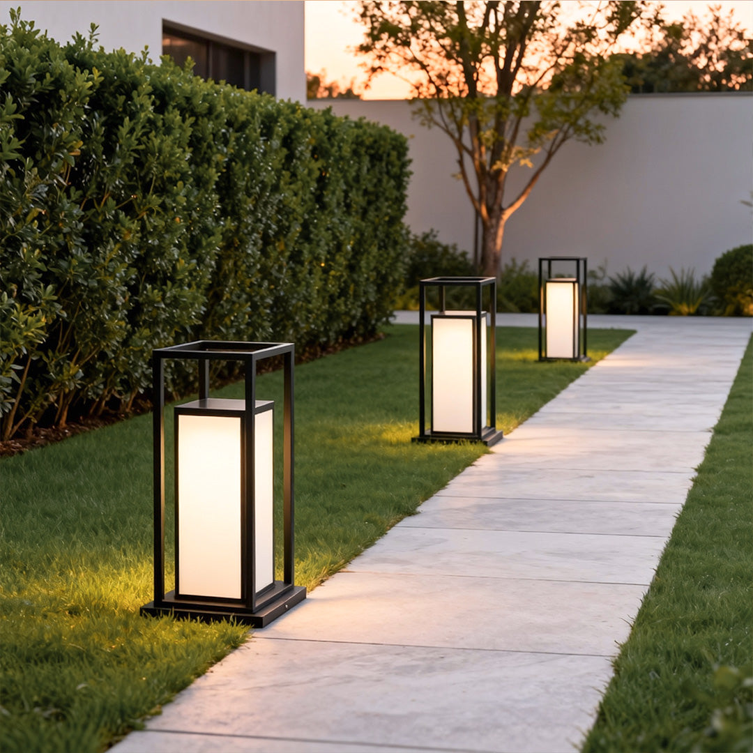 Modern outdoor wall pillar lights placed evenly along hedge-lined outdoor pathway.