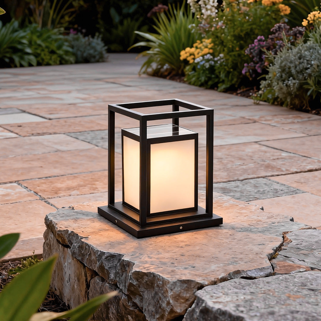 Modern outdoor wall pillar lights displayed on stone platform in landscaped outdoor setting.