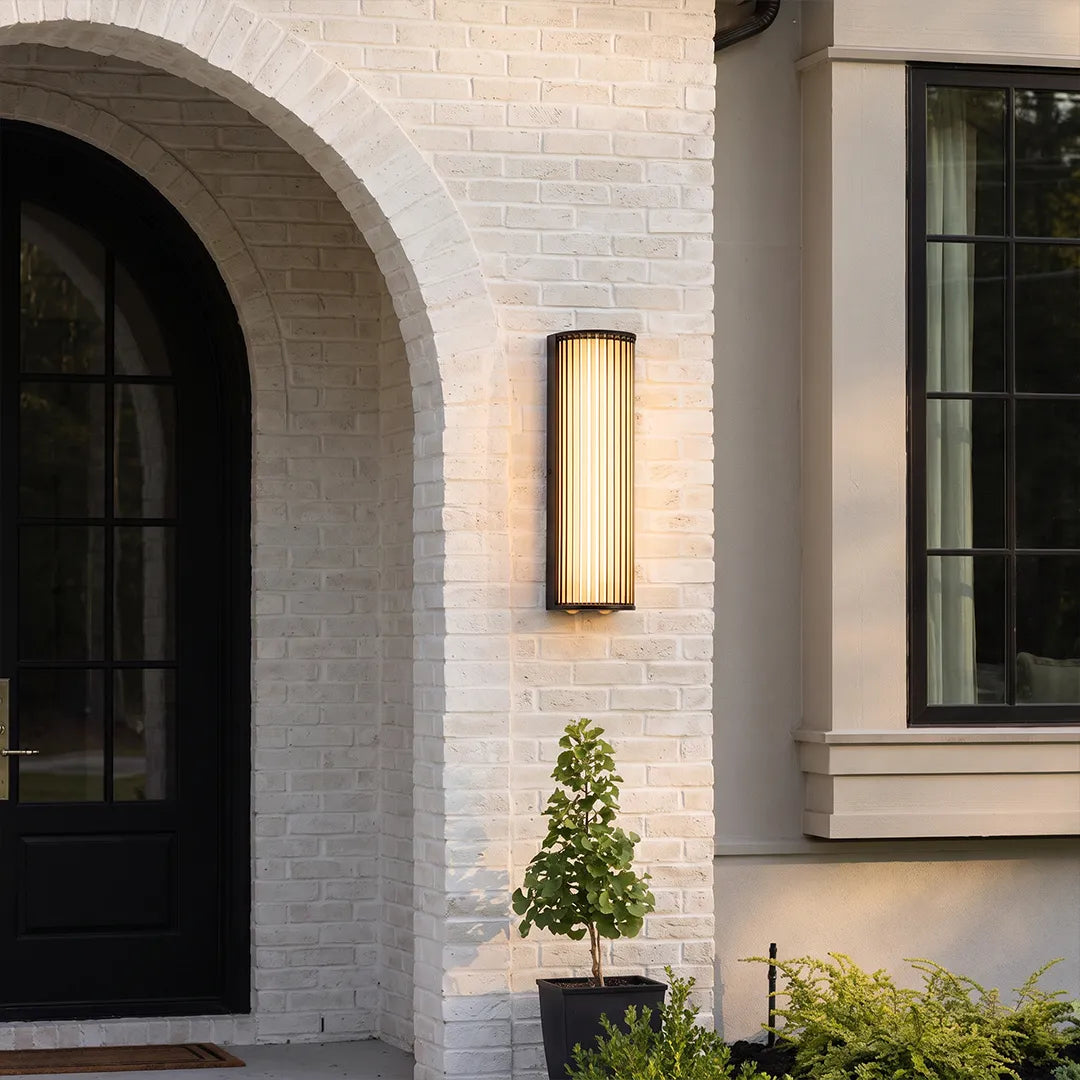 Modern outdoor wall sconce with warm glow beside arched home entrance