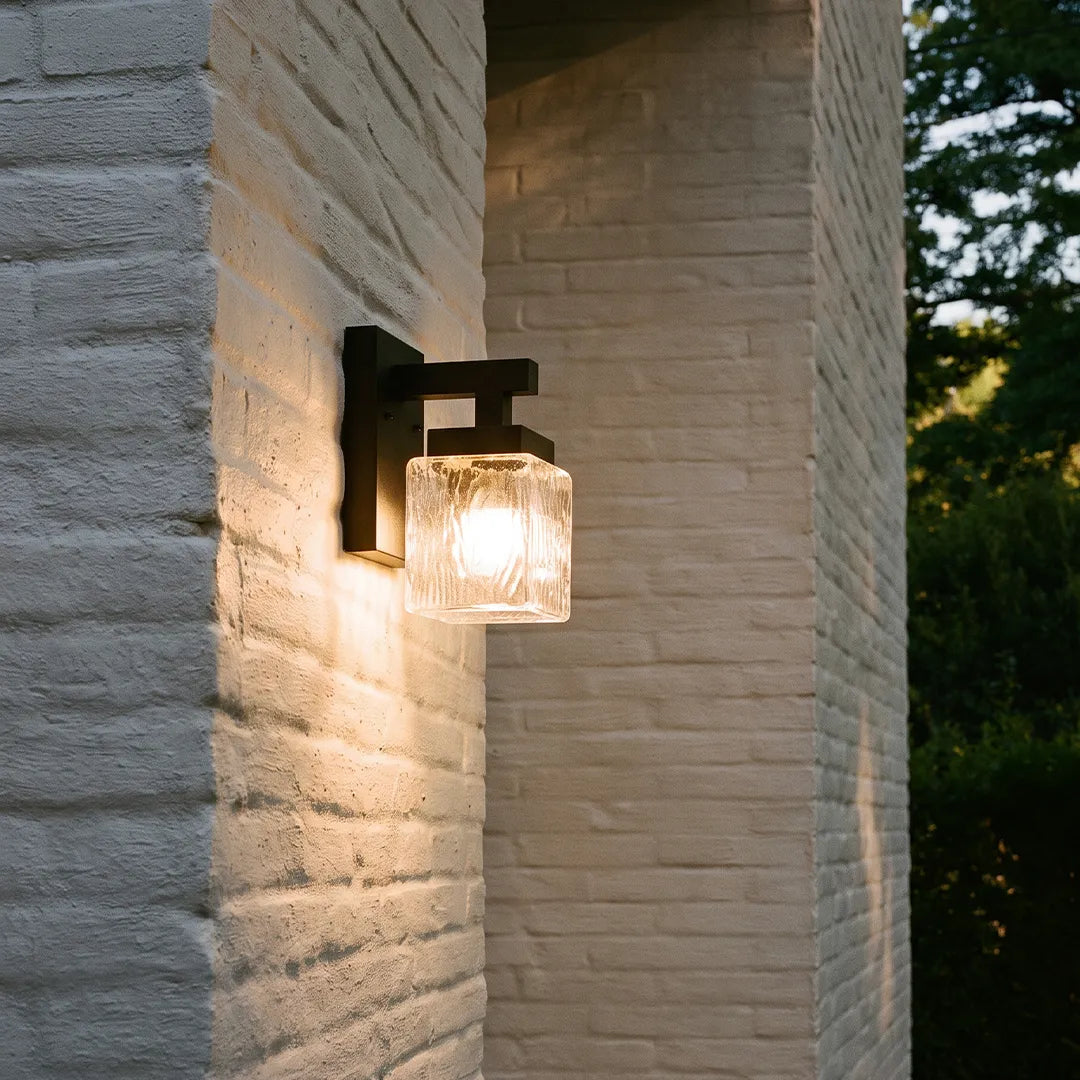 Modern outdoor wall sconce with textured glass shade and warm glow on brick wall