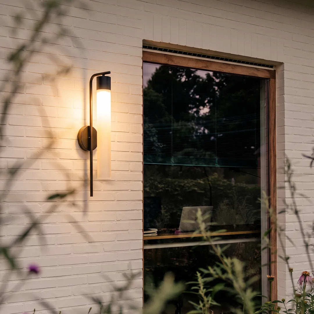 Modern outdoor wall sconce with black frame and warm glow beside glass door