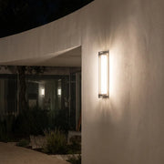 Modern outdoor wall sconce with silver frame and warm glow on concrete wall