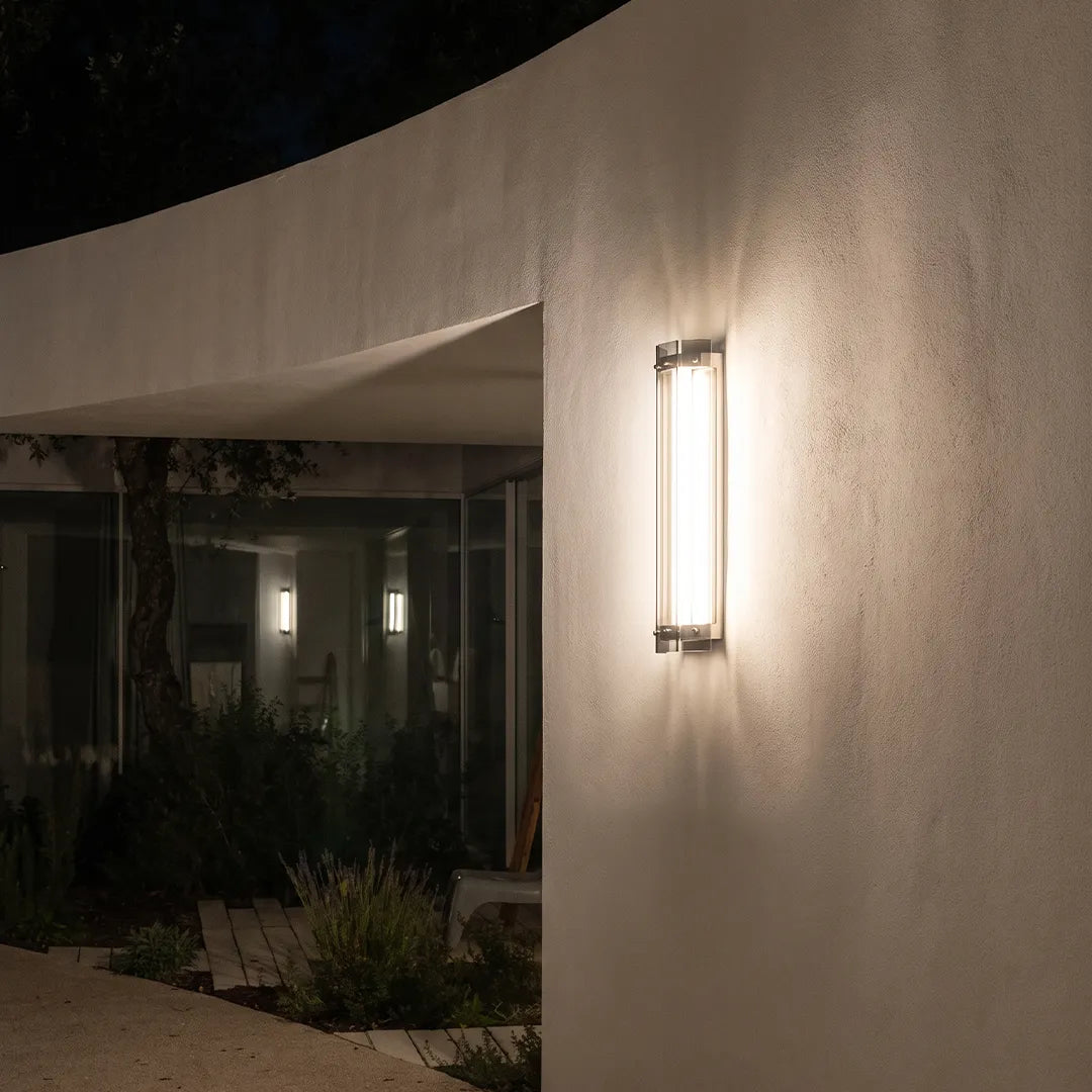 Modern outdoor wall sconce with silver frame and warm glow on concrete wall