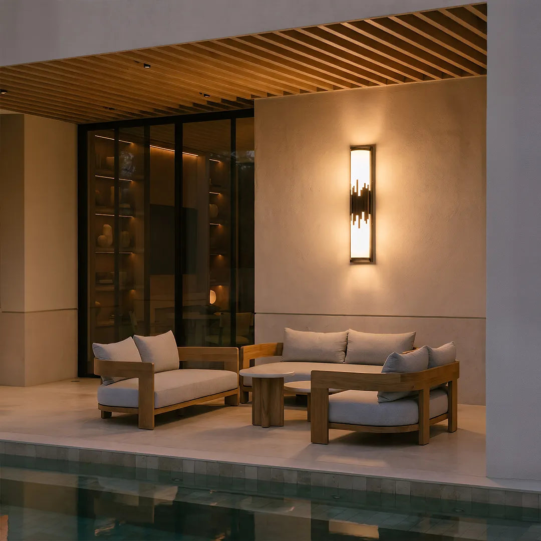 Modern outdoor wall sconce with warm glow beside covered patio lounge seating