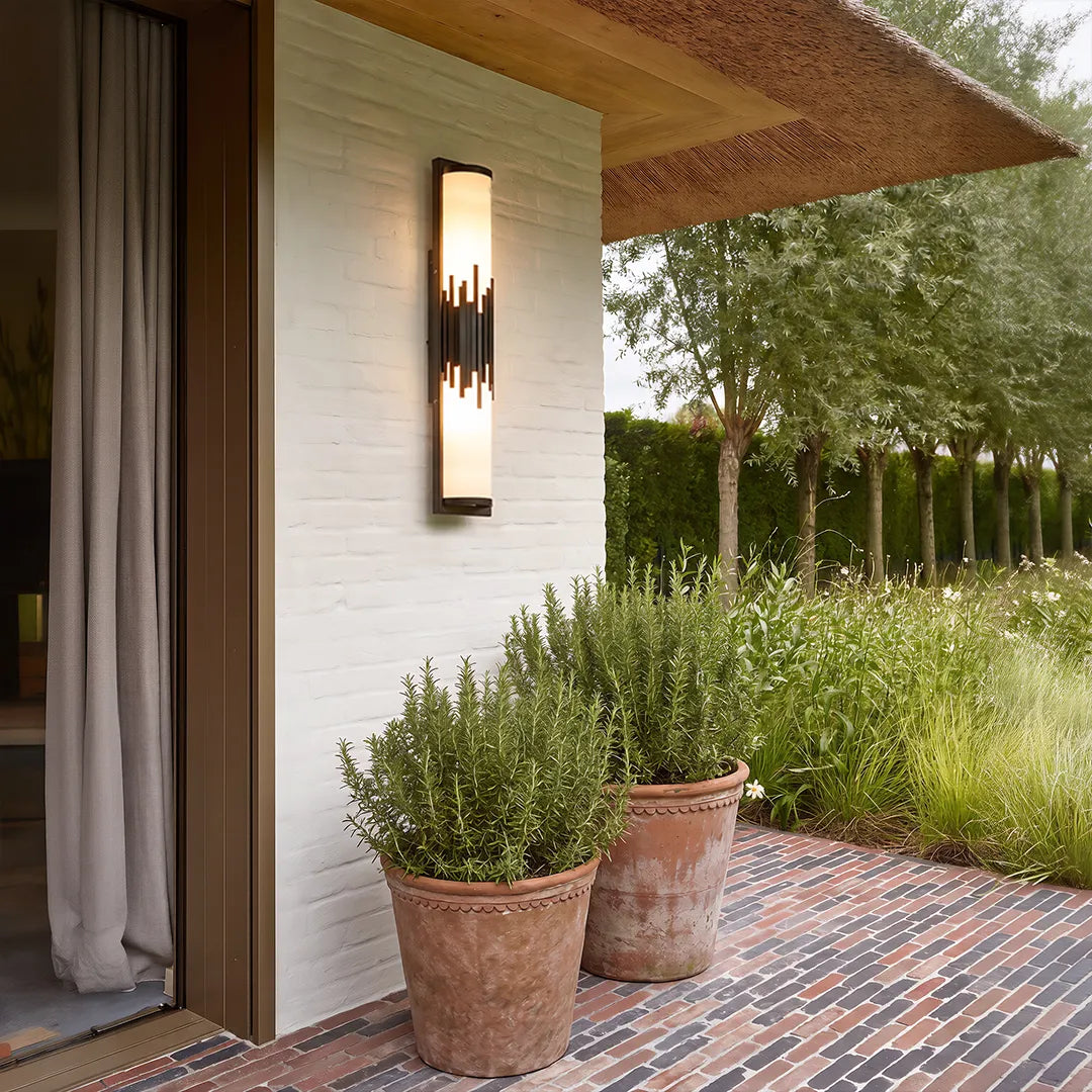 Modern outdoor wall sconce with gold accents beside covered porch and garden