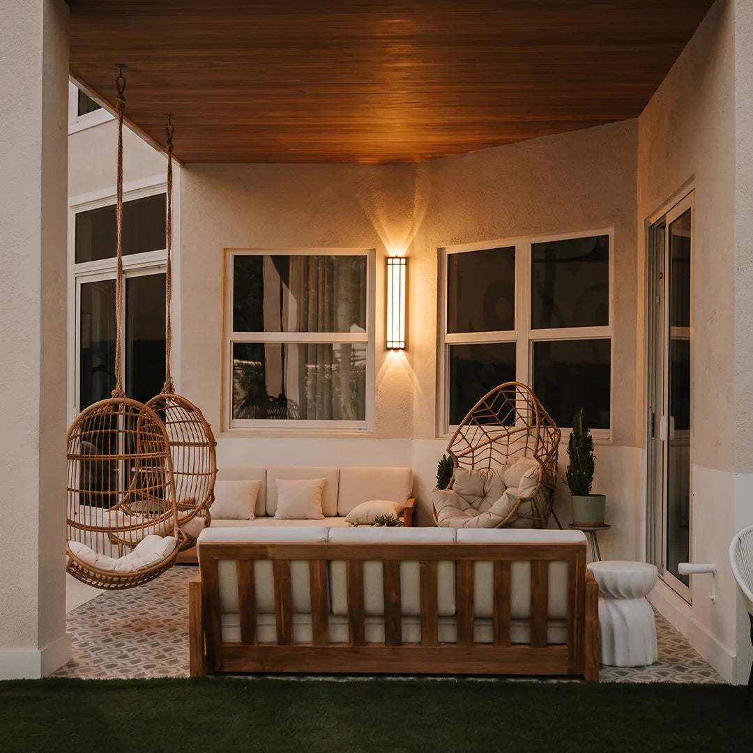 Modern outdoor wall sconce with warm glow beside covered porch seating