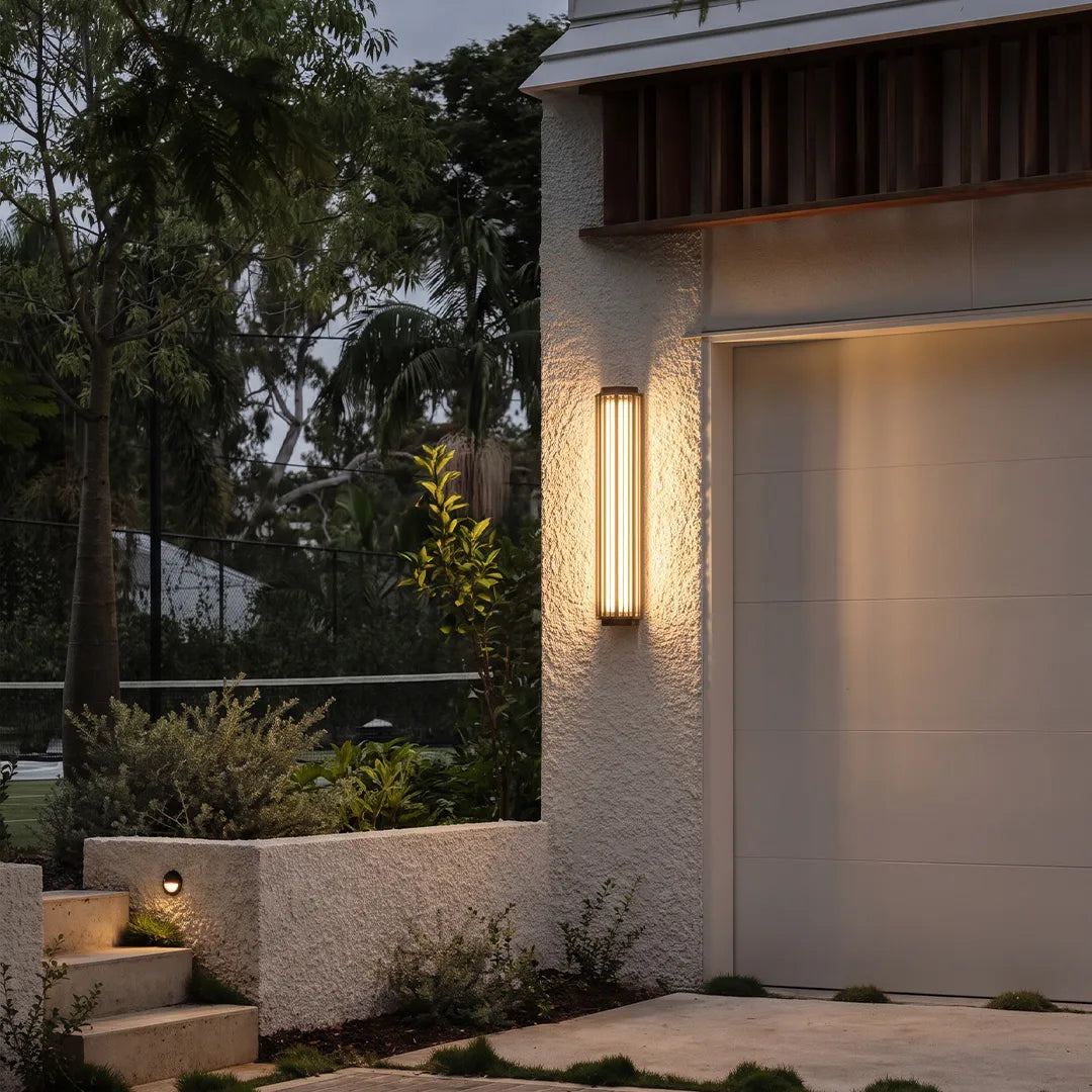 Modern outdoor wall sconce illuminating garage exterior and landscaped garden
