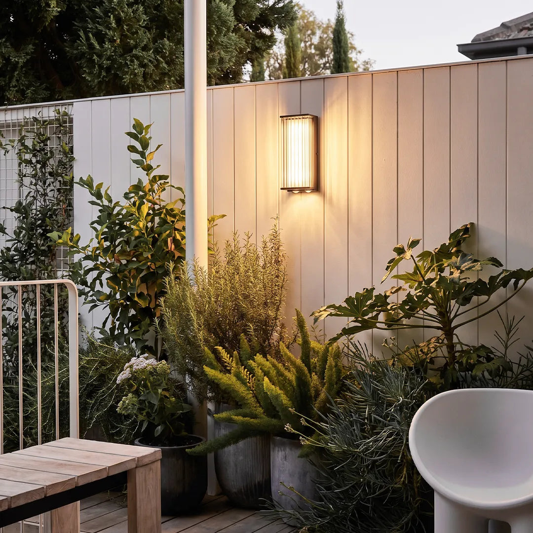Modern outdoor wall sconce illuminating garden fence and patio plants
