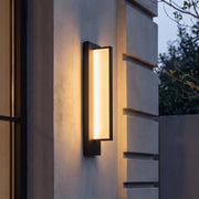 Modern outdoor wall sconce with black frame and warm glow on home exterior