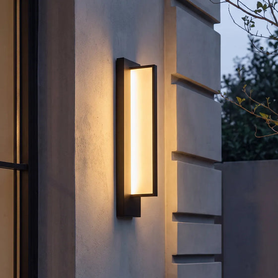 Modern outdoor wall sconce with black frame and warm glow on home exterior