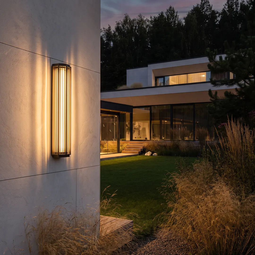Modern outdoor wall sconce with warm glow beside contemporary home and garden