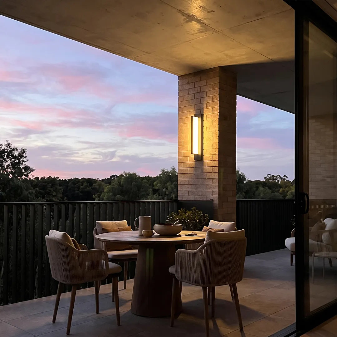 Modern outdoor wall sconce illuminating patio dining area at sunset