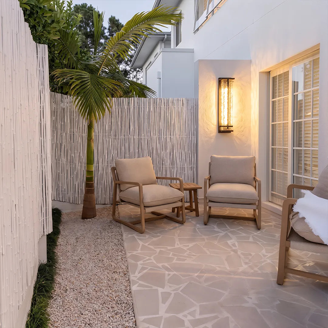 Modern outdoor wall sconce beside patio lounge chairs and garden plants