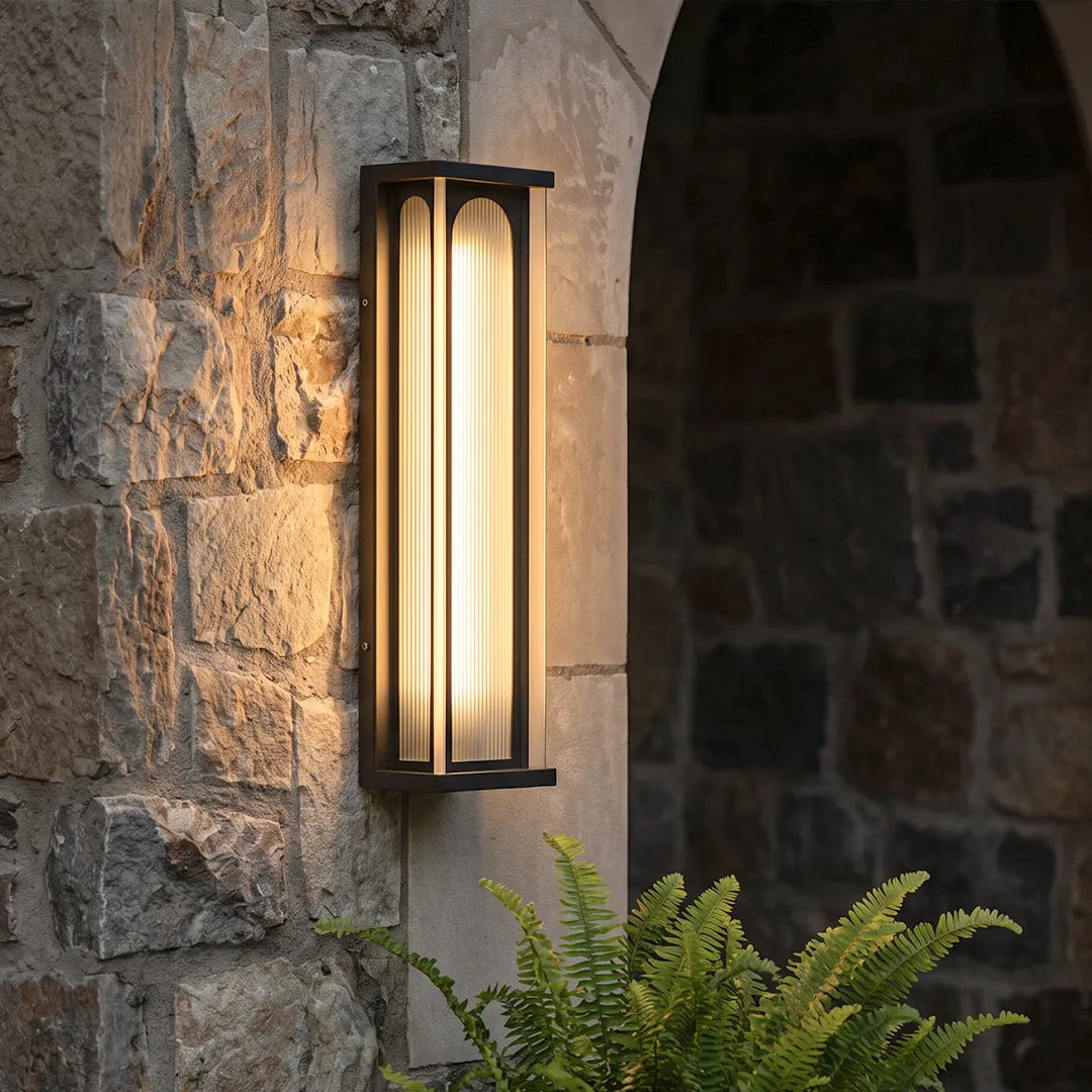 Modern outdoor wall sconce with warm lighting on stone wall beside garden plants