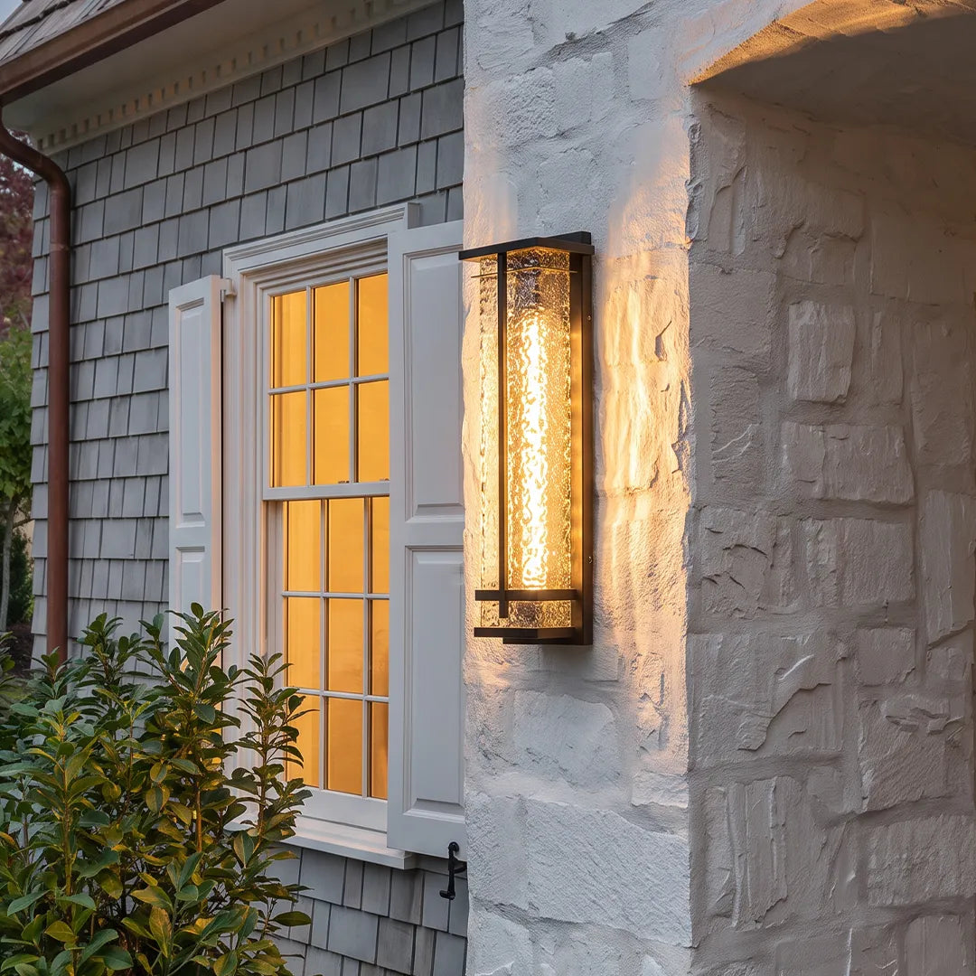 Modern outdoor wall sconce with textured glass and warm glow on stone house exterior