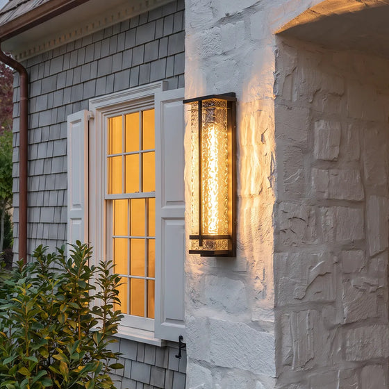 Modern outdoor wall sconce with textured glass and warm glow on stone house exterior