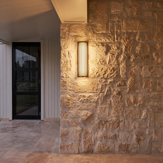 Modern outdoor wall sconce with ribbed glass shade and warm glow on stone wall
