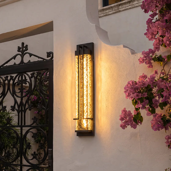 Modern outdoor wall sconce with warm textured glass beside garden flowers