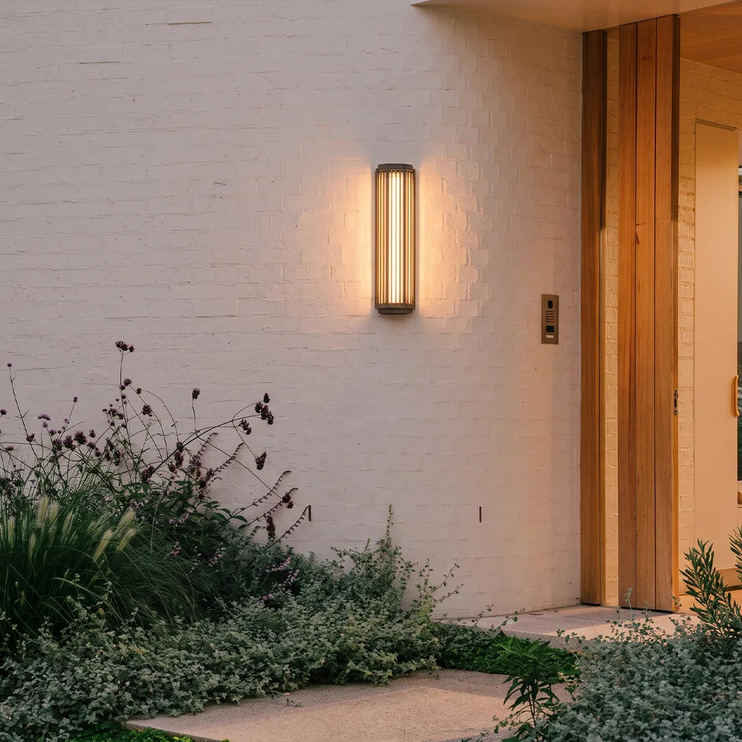 Modern outdoor wall sconce with warm glow beside home entrance and garden plants