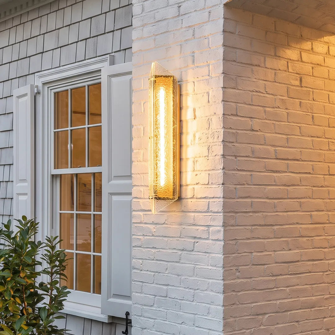 Modern outdoor wall sconce with gold frame and textured glass on white brick wall