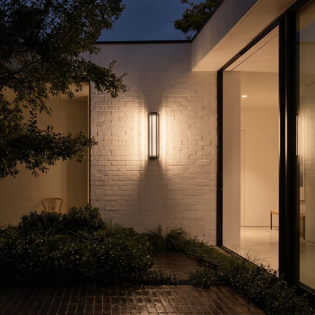 Modern outdoor wall sconce with warm glow on white brick wall beside garden