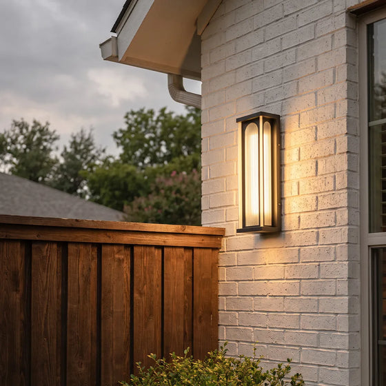 Modern outdoor wall sconce with warm glow on white brick house exterior