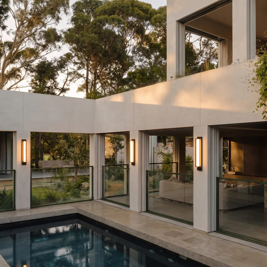 Modern outdoor wall sconces with warm glow beside pool and glass doors