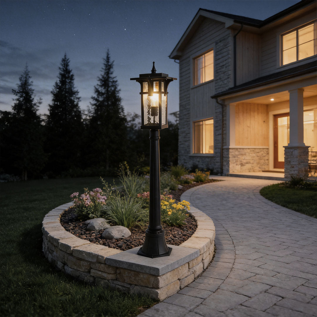 Modern path light with black metal frame casting soft light on a landscaped driveway entrance.