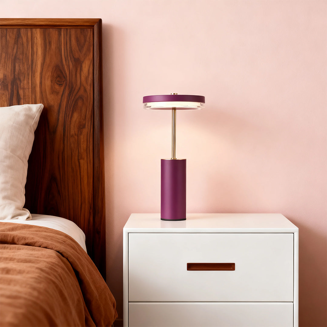 Modern plum and gold cylinder table lamps on a white bedside table in a cozy bedroom setting.