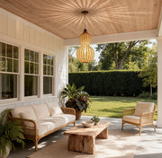 Modern rattan pendant light hanging over a cozy covered patio seating area, creating a warm and natural outdoor ambiance.