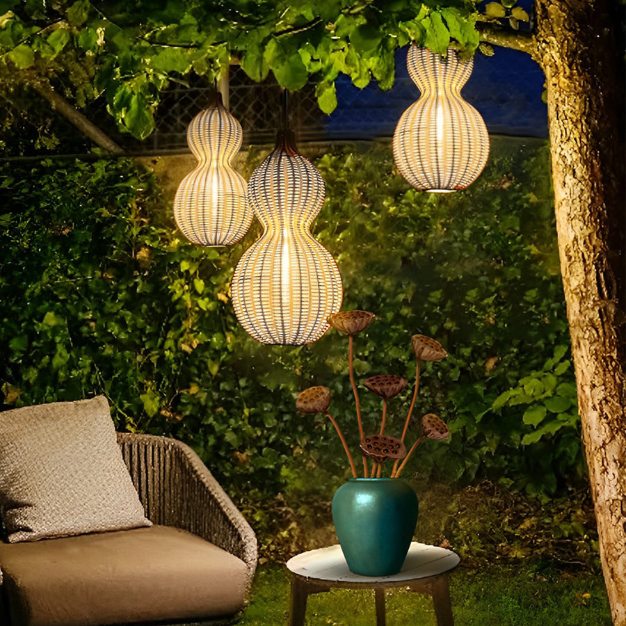 Modern rattan pendant light hanging from tree branches, casting decorative shadows in a lush garden setting at night.
