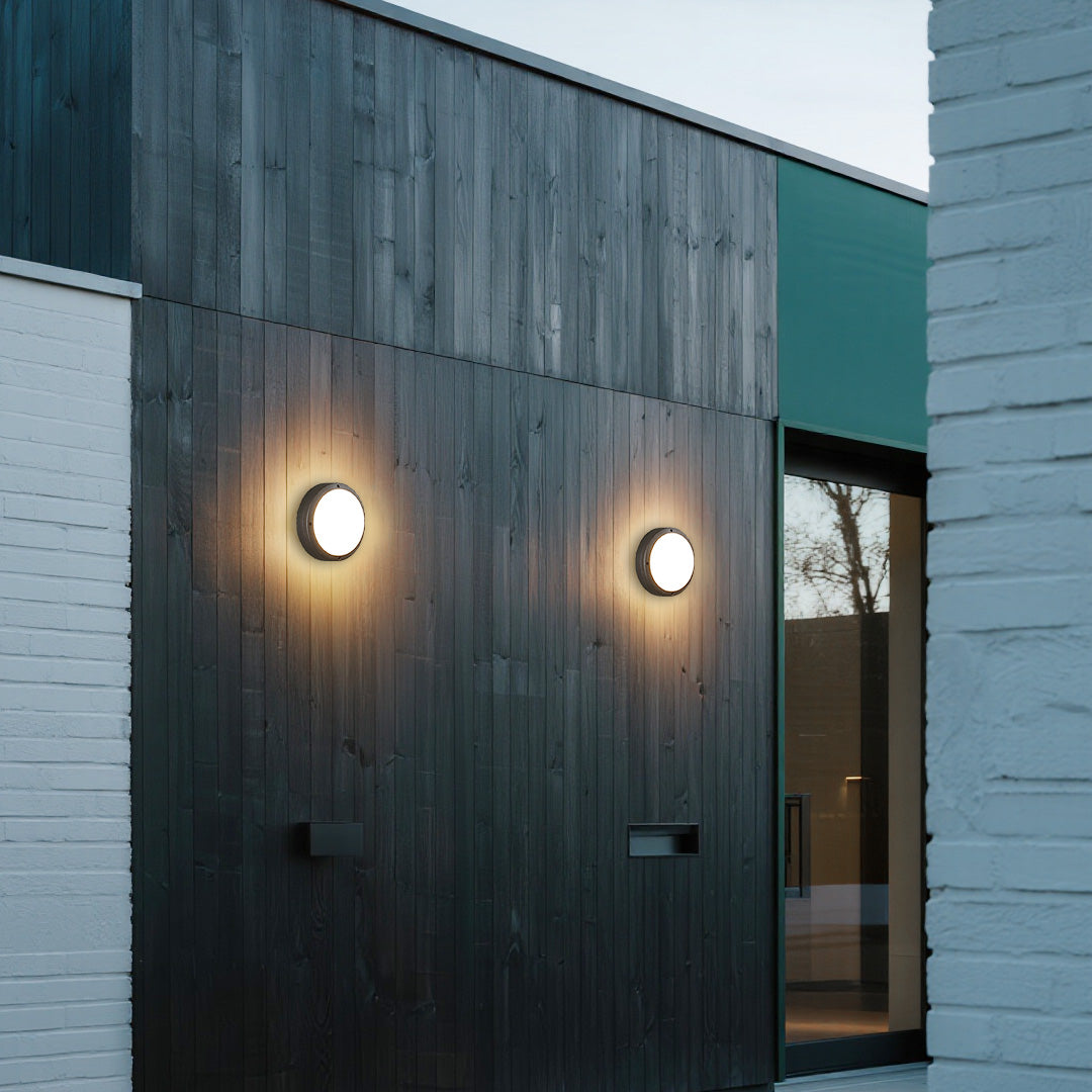 Modern residential entrance enhanced by two glowing round outdoor wall lights on a dark wooden facade.