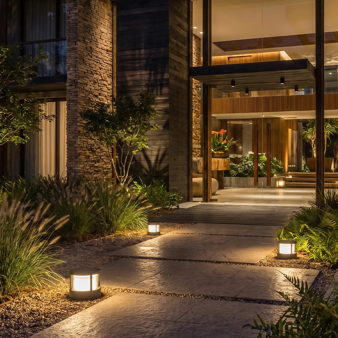 Modern round outdoor post light illuminating a curved garden walkway beside a contemporary home entrance at night.