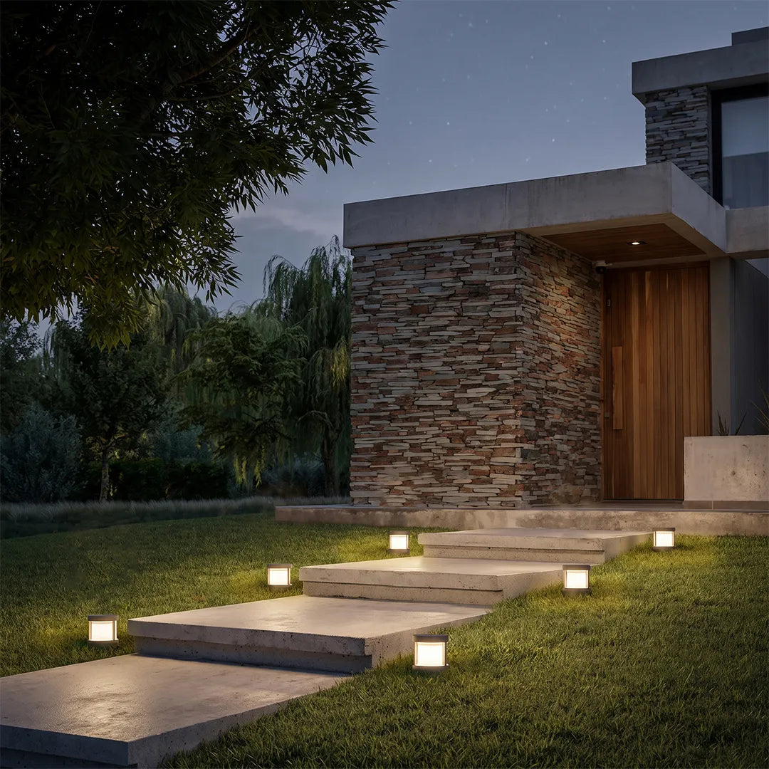 Modern round outdoor post lights lining a stepped lawn pathway in front of a stone-clad contemporary home.