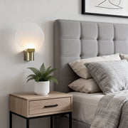 Modern round wall light with a frosted glass shade and gold metal base, mounted beside a cozy bedroom headboard.