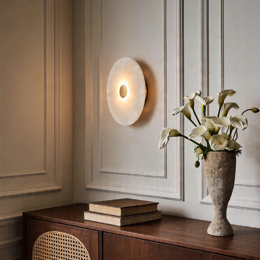 Modern round wall light illuminating a minimalist home space above a dark wood sideboard ok.